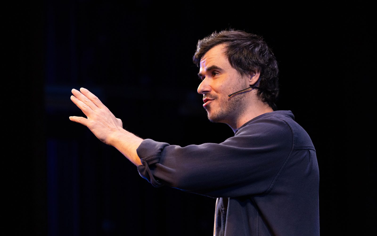 Sam Kissajukian seen in profile in a blue button down shirt, stretches his arm out in front of him.