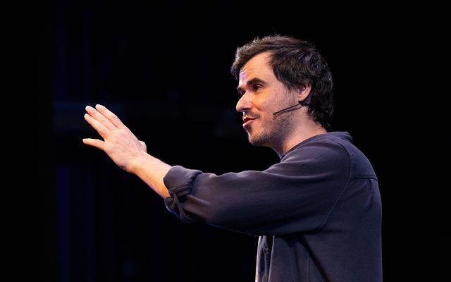 Sam Kissajukian seen in profile in a blue button down shirt, stretches his arm out in front of him.