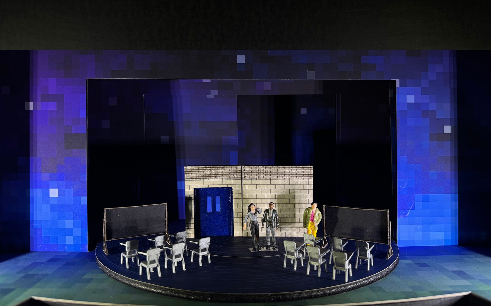 Set model of Wonder with two sets of six chairs facing blackboards, with three figurines standing in front of a cinderblock wall.