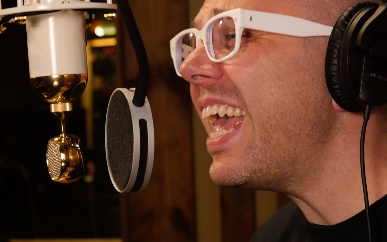 Ian Axel in white glasses sings into a studio microphone.