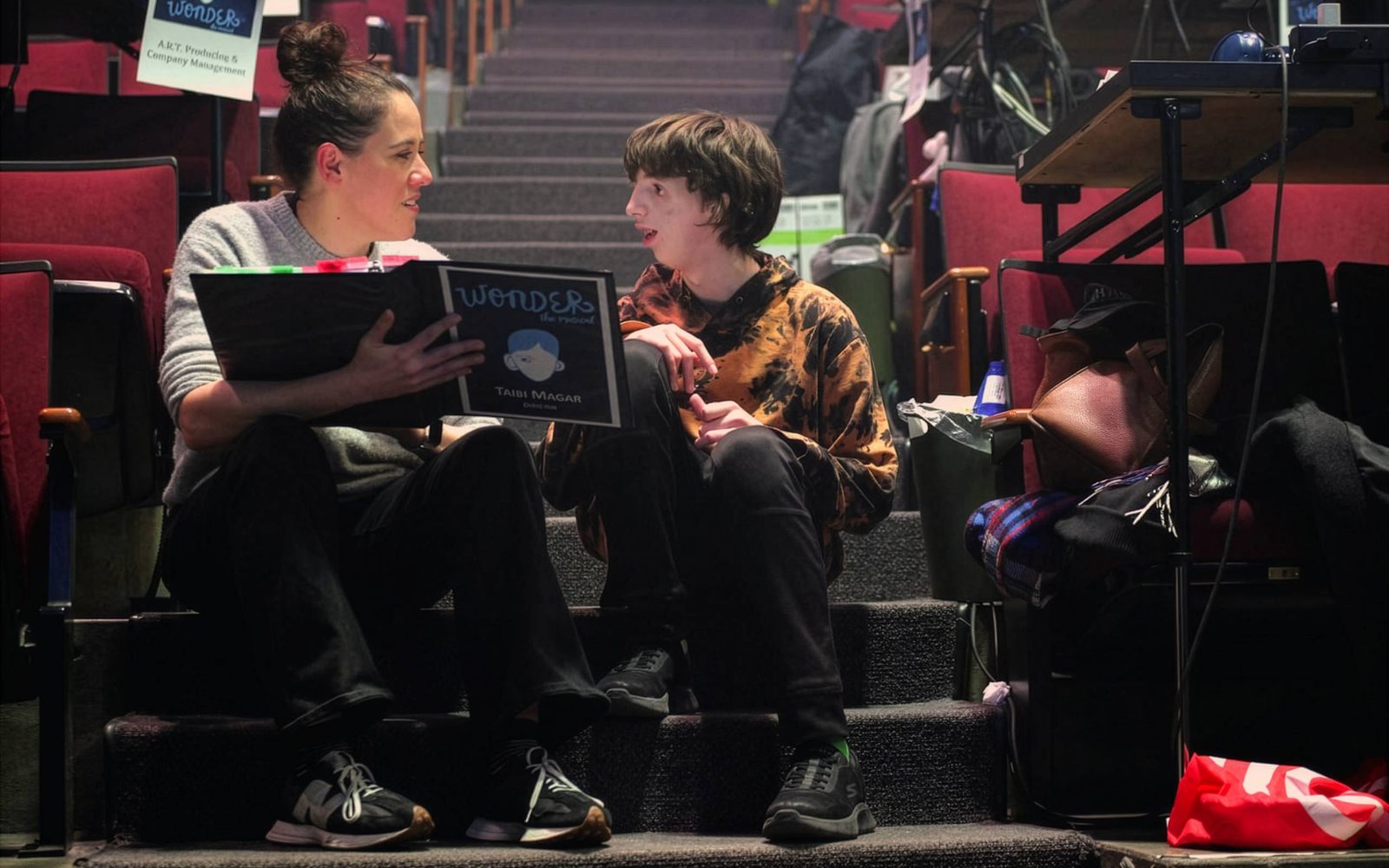Taibi Magar shows a script to Garrett McNally, sitting next to each other on carpeted steps.