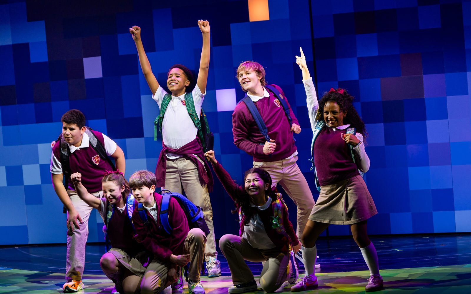Members of the cast of Wonder pose at the front of the stage, some crouching and others with arms raised.