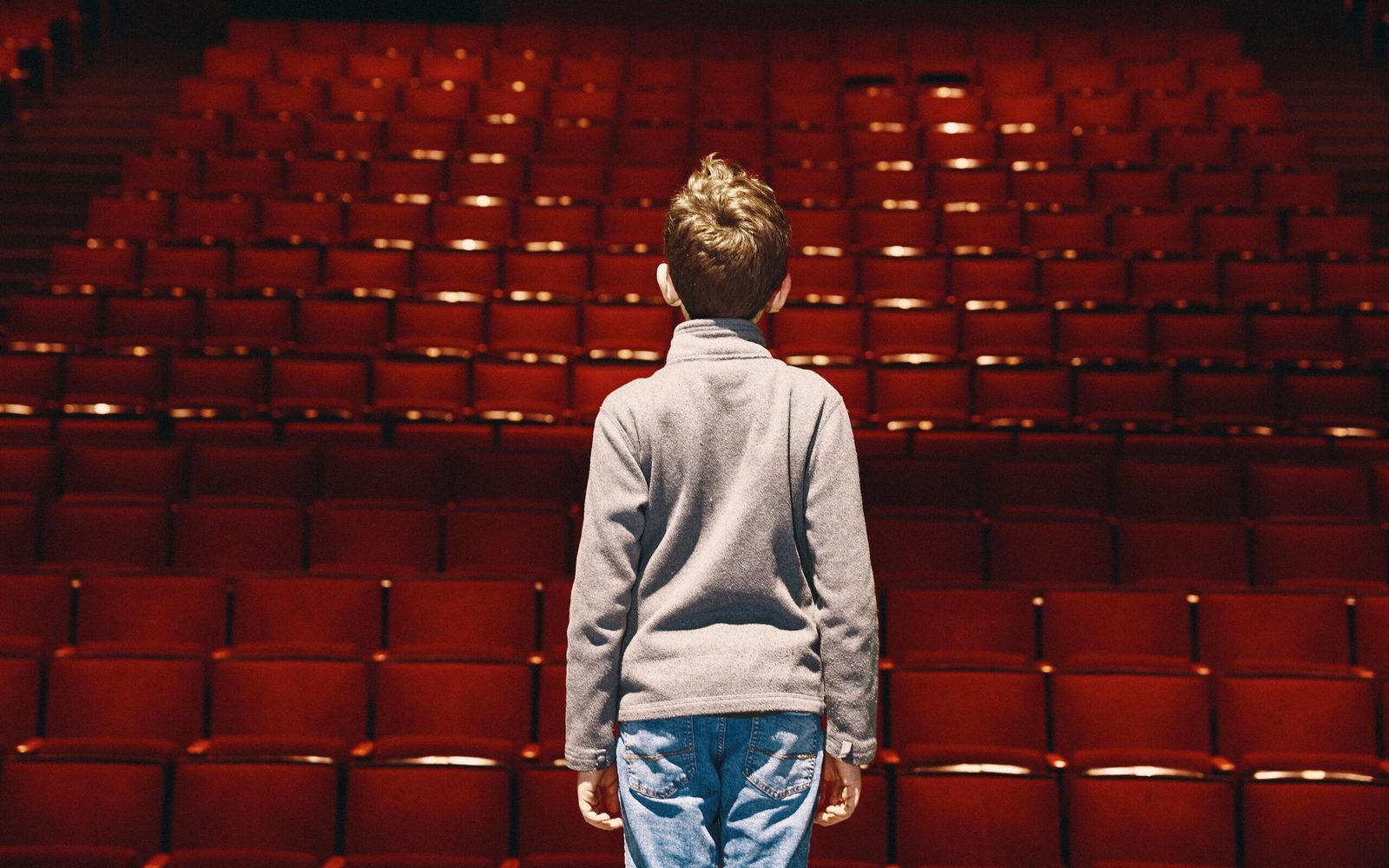 The back of Max Voehl, in a grey quarter-zip and jeans, as he faces rows of red chairs.