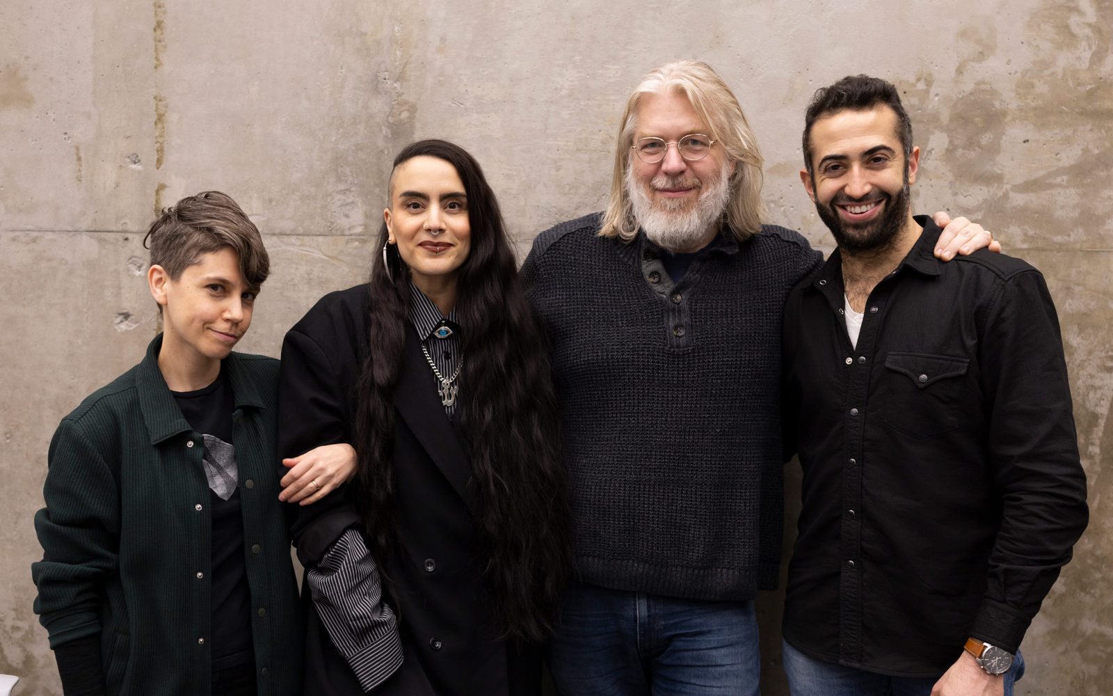 Jen Silverman, Sonyah Tayeh, Dave Malloy, and Or Matias, all dressed in black, pose together in front of a texture concrete wall.