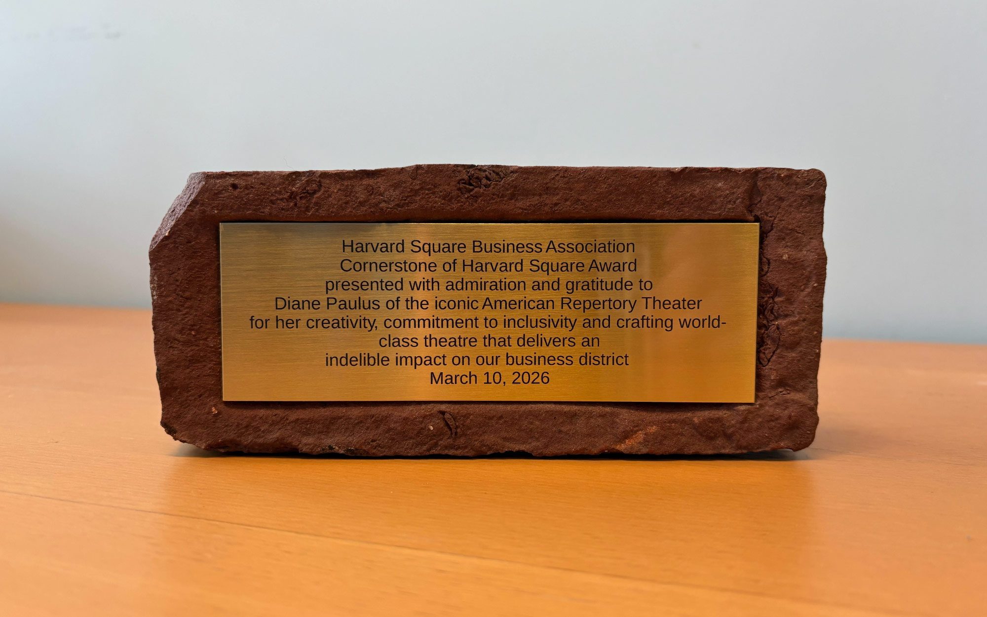 A red brick with a plaque installed on it that reads, “Harvard Square Business Association Cornerstone of Harvard Square Award presented with admiration and gratitude to Diane Paulus of the iconic American Repertory Theater for her creativity, commitment to inclusivity and crafting world-class theatre that delivers an indelible impact on our business district March 10, 2026.”